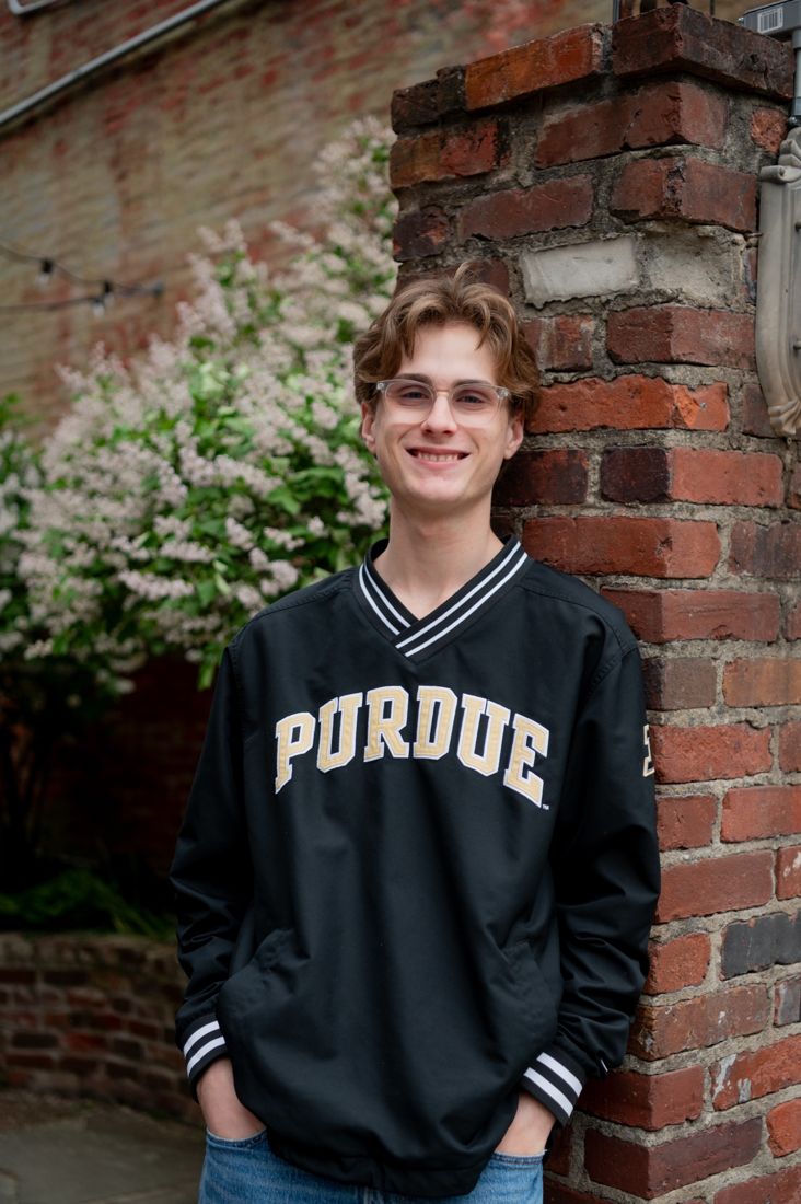 Joey smiling in a Purdue jacket by a brick pillar